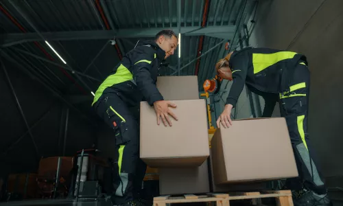 Two people lifting boxes in a warehouse